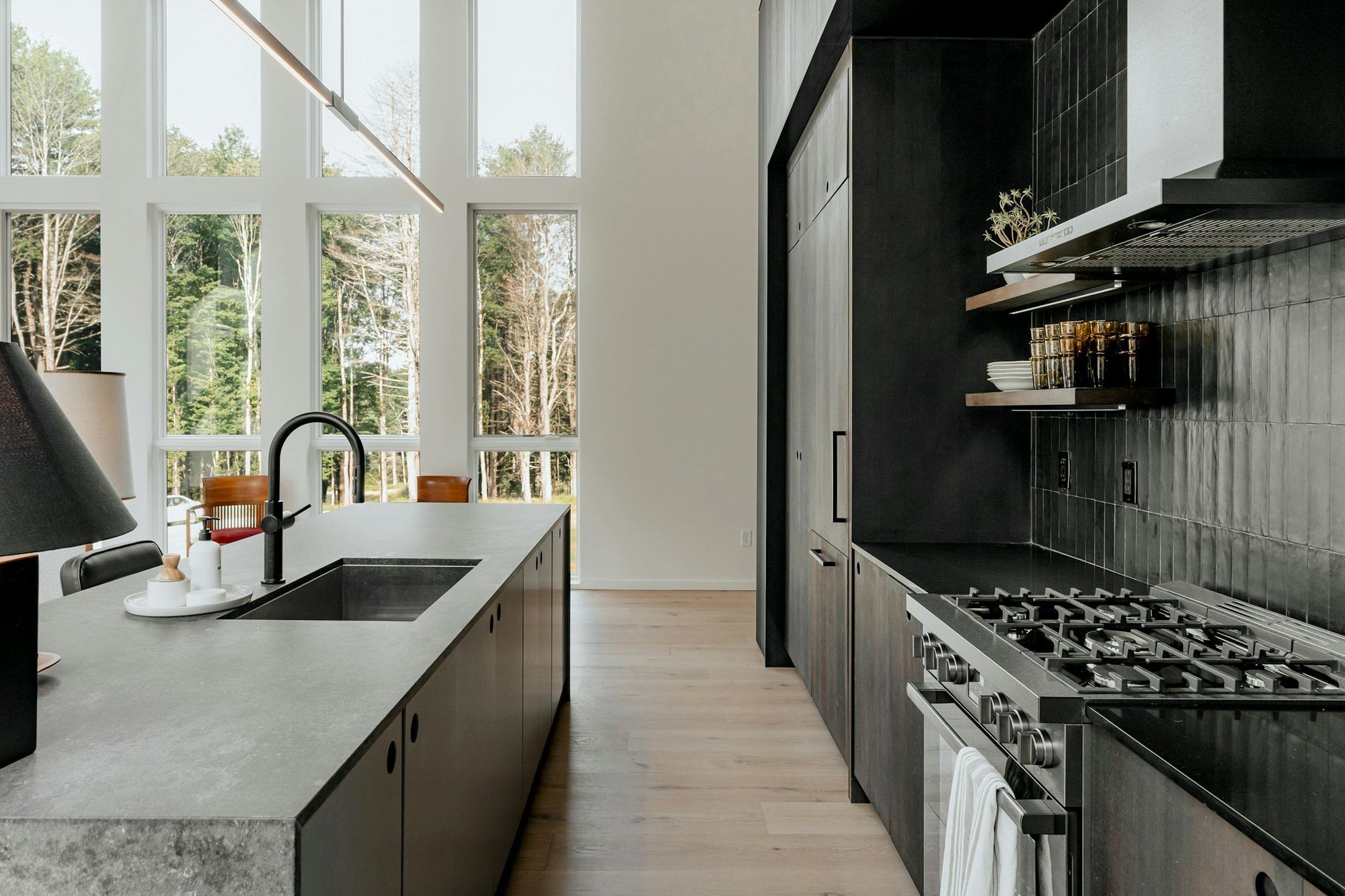 A black kitchen with stone counters and tall windows